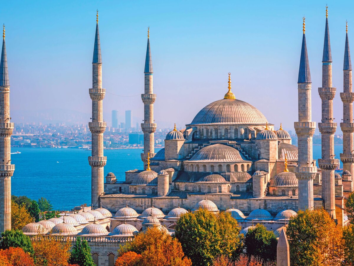 Die berühmte Blaue Moschee in Istanbul, mit ihren sechs Minaretten und der großen Kuppel, im Vordergrund herbstliche Bäume und im Hintergrund das blaue Wasser des Bosporus. | © railtour